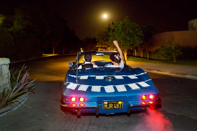Bride and groom riding off in a blue corvette. 
