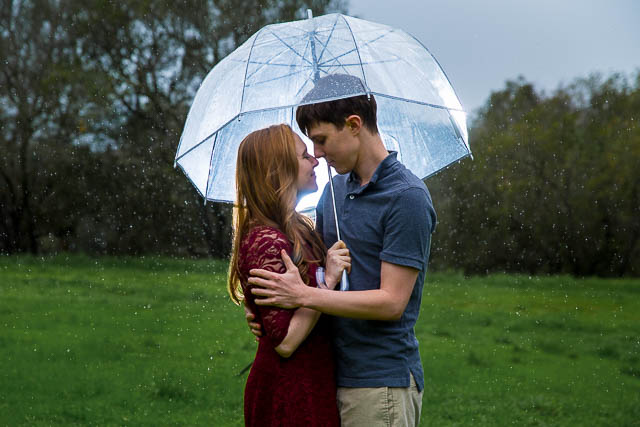 Engaged couple holding each other under the clear umbrella in the rain at Hans Christian Andersen Park in Solvang California.