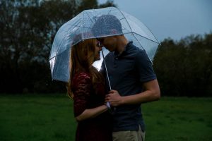 Engaged couple holding each other under the clear umbrella in the rain at Hans Christian Andersen Park in Solvang California.