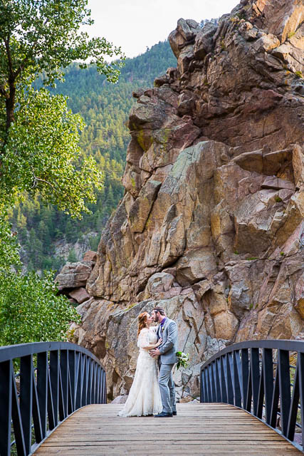 Newlyweds embracing on a bridge on a Boulder, Colorado trail in the Rockies mountains.