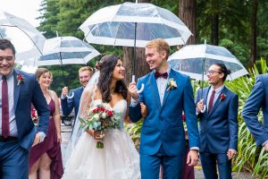 Bride and groom with their bridal party walking in the rain with umbrellas in Rotorua, New Zealand.