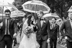 Bride and groom with their bridal party walking in the rain with umbrellas in Rotorua, New Zealand.