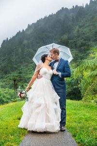Bride and groom using a clear umbrella to shield them from the rain during their Blue Lake Rotorua New Zealand wedding Day After photos.