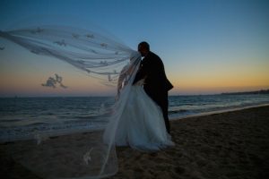 Romantic sunset photo of couple on the beach with a cathedral veil.